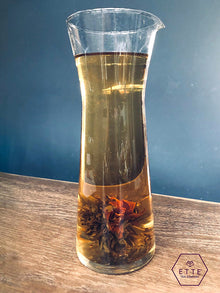 Clear glass carafe with tea leaves and liquid on a wooden surface with a blue background