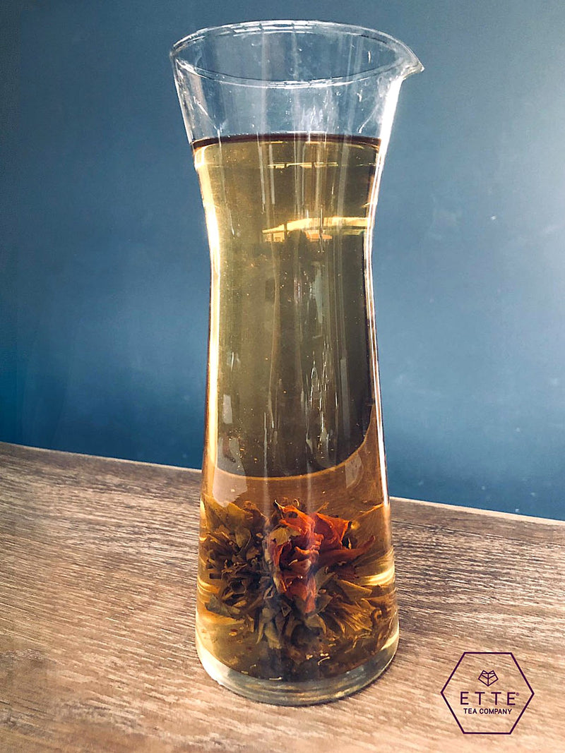 Clear glass carafe with tea leaves and liquid on a wooden surface with a blue background