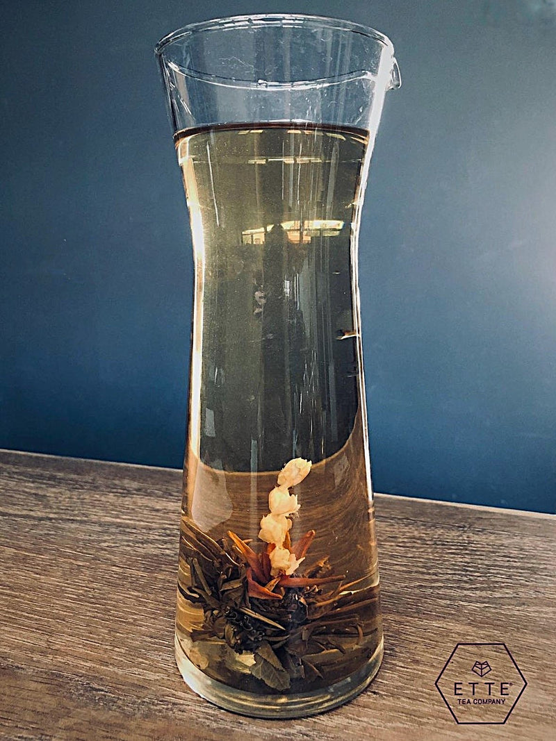 Glass carafe with tea leaves and liquid on a wooden surface, branded 'ETTE Tea Company'.