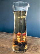 Glass carafe with floral tea on a wooden surface against a blue wall