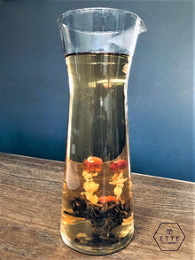Glass carafe with floral tea on a wooden surface against a blue wall