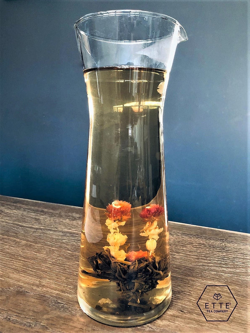 Glass carafe with floral tea on a wooden surface against a blue wall