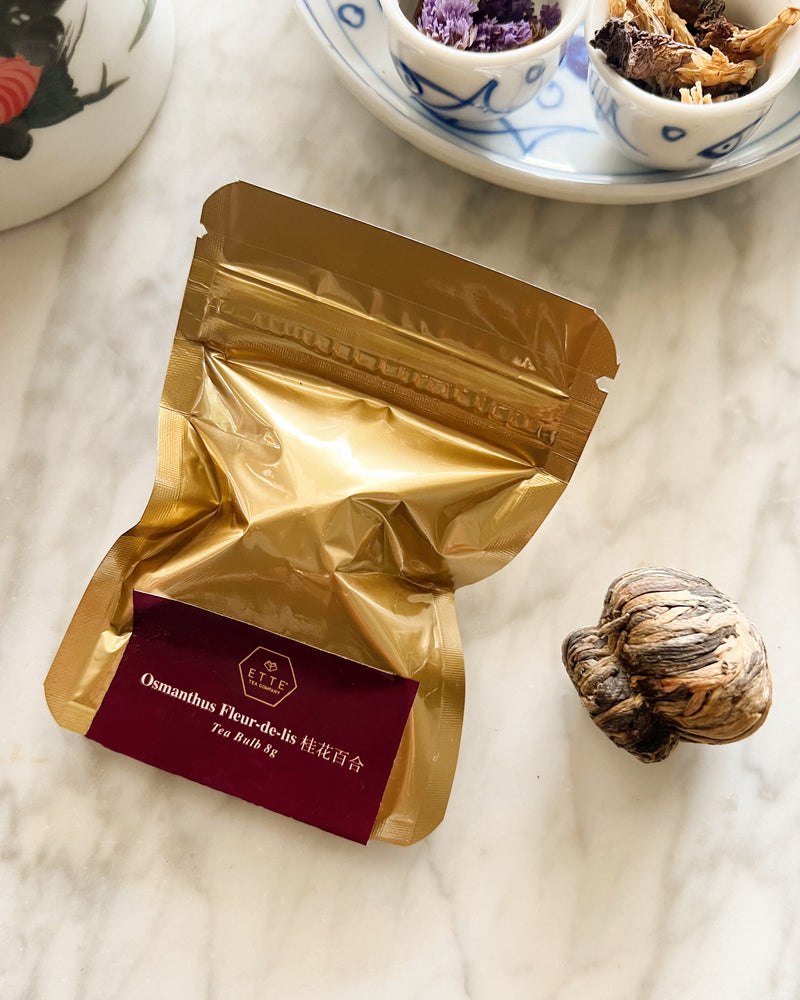 Gold tea bag with a red label on a marble surface, with a teacup and saucer in the background.