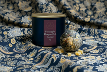 Tea ball packaging with pineapple dragon orb on a decorative fabric background